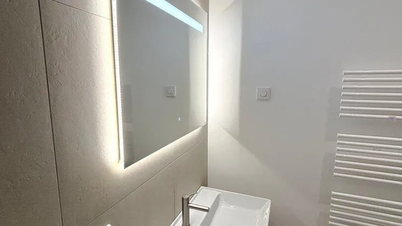 Modernes Badezimmer mit beleuchtetem Spiegel, Einzelwaschbecken und Handtuchheizkörper.