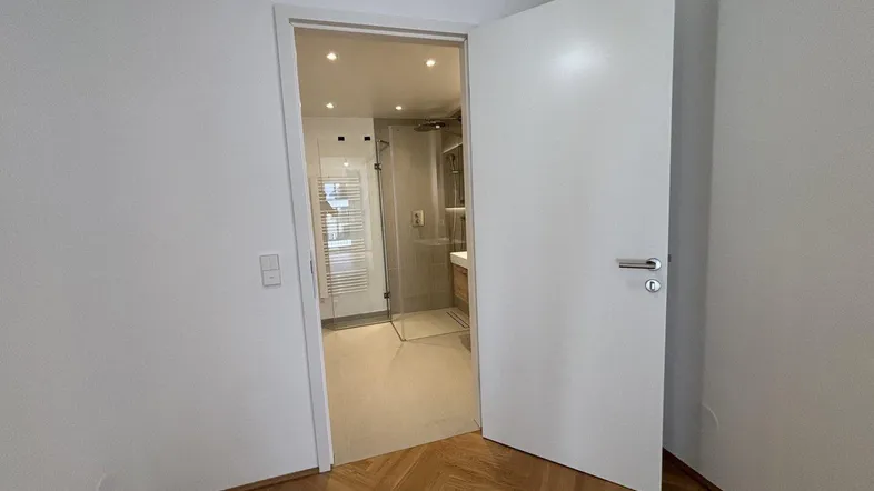 Blick durch eine offene Tür in ein modernes Badezimmer mit Duschkabine und Waschtisch.