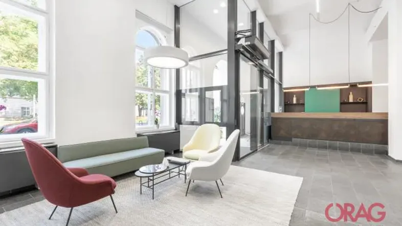 Heller Empfangsbereich mit modernen Sitzgelegenheiten, großen Fenstern und dunklem Fliesenboden.