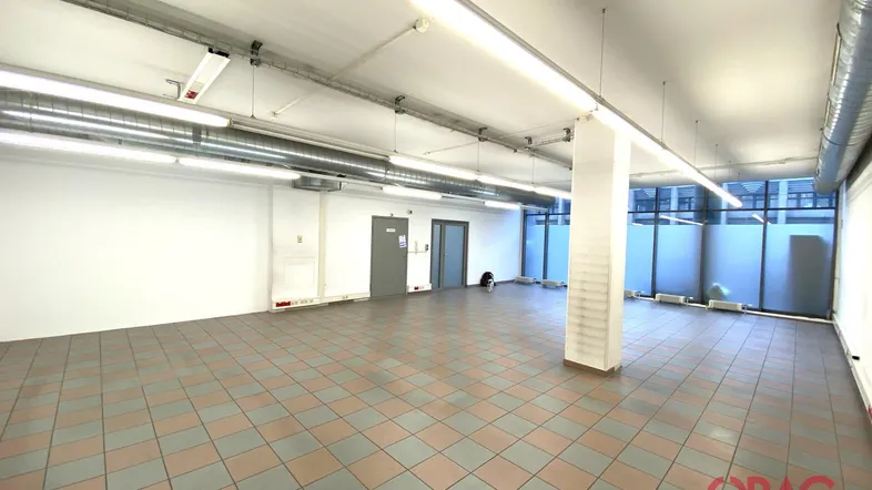 Großer, leerer Gewerberaum mit Fliesenboden, hohen Decken und sichtbaren Lüftungsrohren.