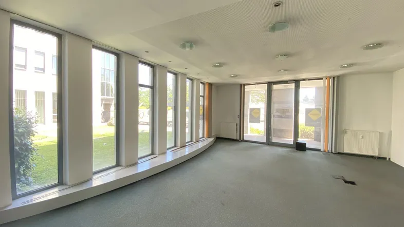 Geräumiger Büroraum mit großen Fenstern, die viel Tageslicht hereinlassen und Blick ins Grüne bieten.