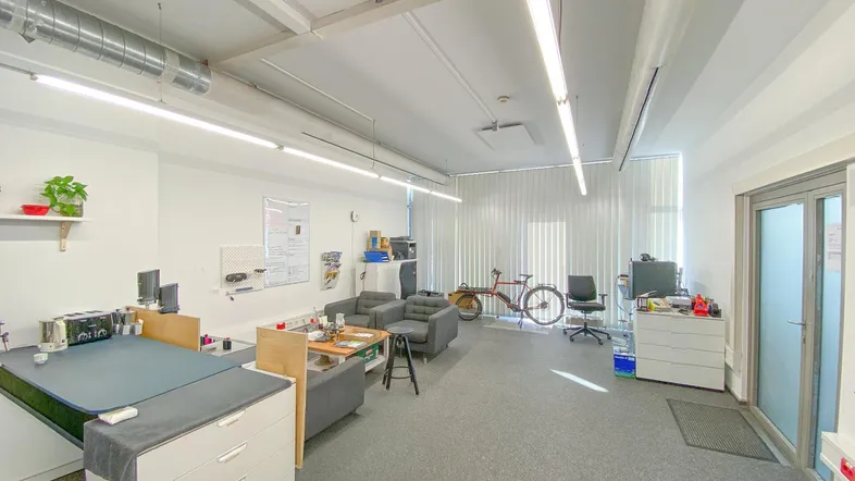 Helles und geräumiges Büro mit mehreren Arbeitsplätzen, einem Loungebereich und großen Fenstern.