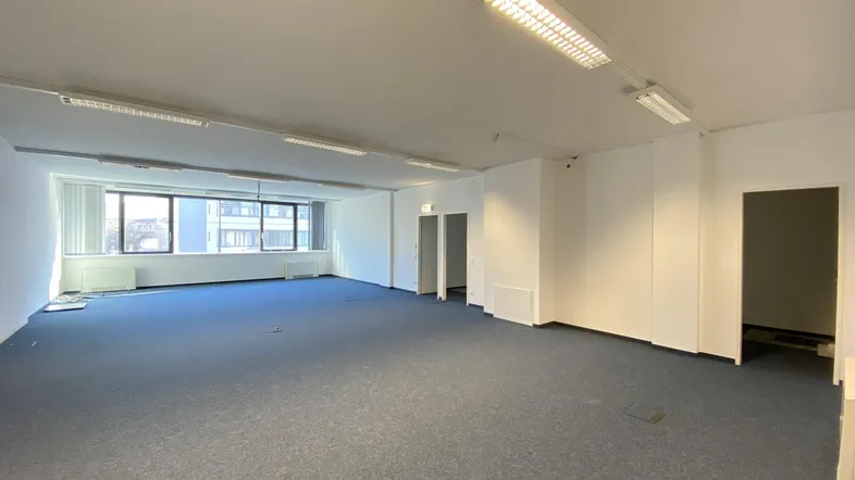 Großes, leeres Büro mit blauem Teppichboden und großen Fenstern, bereit zur Renovierung.