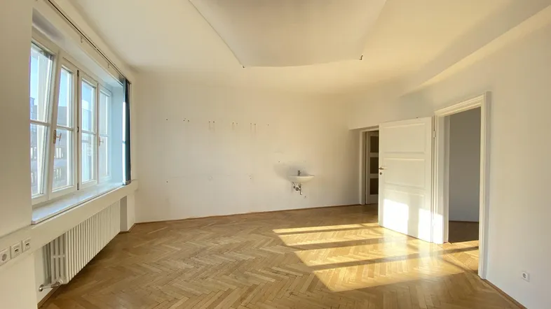 Heller Büroraum mit Fischgrätparkett, großen Fenstern und einem kleinen Waschbecken an der Wand.