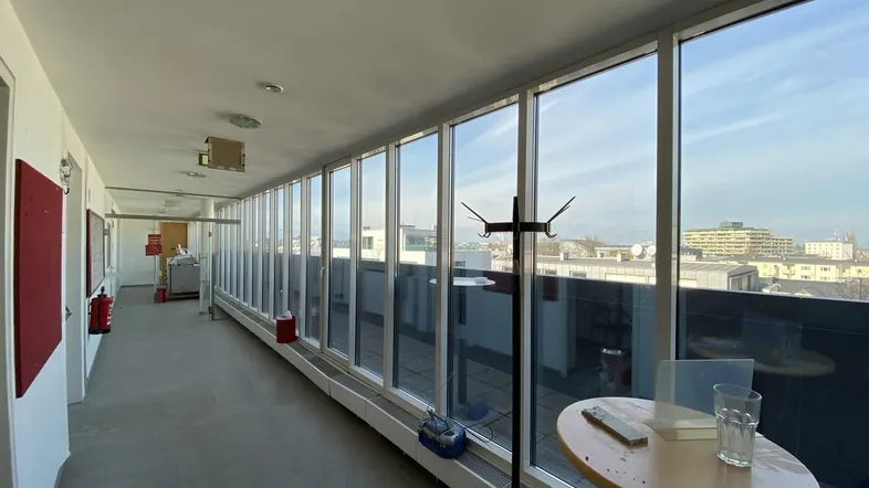 Heller Korridor mit großen Fenstern, die viel Tageslicht hereinlassen und einen weiten Blick auf die Stadt bieten.