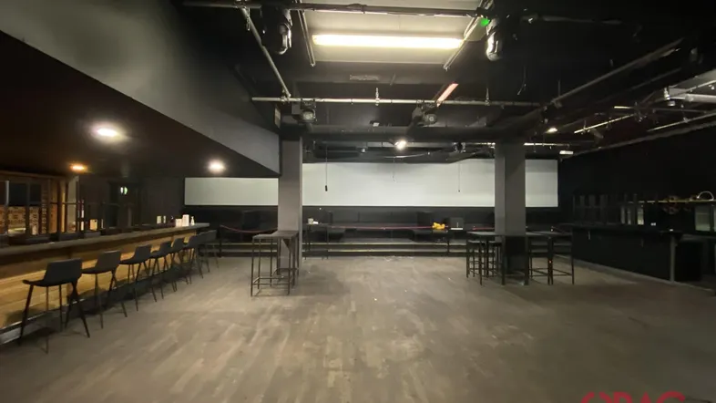 Großer Veranstaltungsraum mit dunkler Decke, Holzboden und einer langen Bar, bereit für Events.