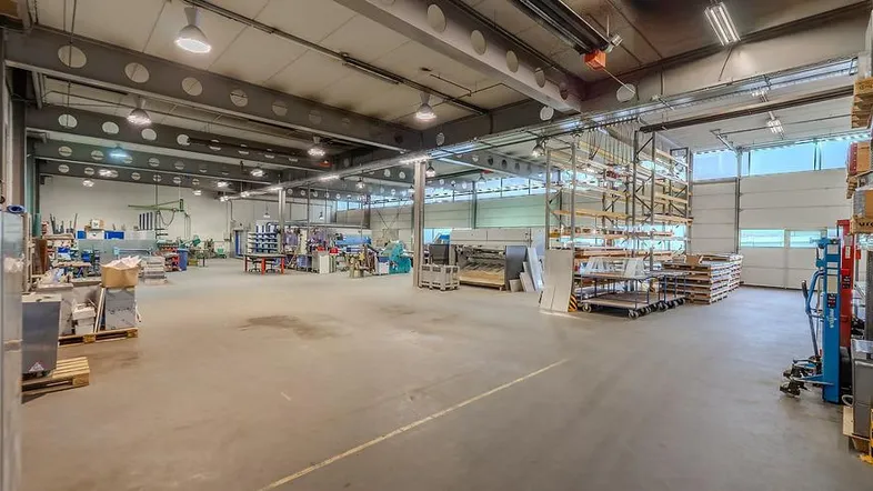 Geräumige Lagerhalle mit hoher Decke, Betonboden und industrieller Beleuchtung, ideal für Produktion und Lagerung.