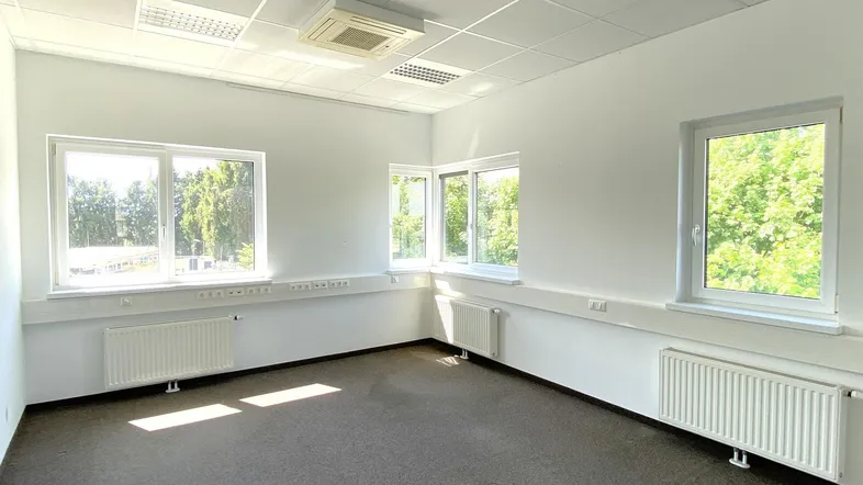 Helles, leeres Büro mit Teppichboden, großen Fenstern und Klimaanlage, ideal für gewerbliche Nutzung.