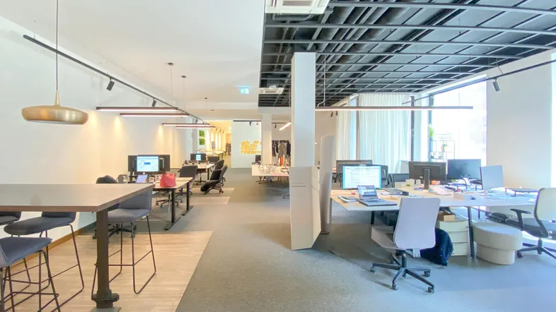 Großes, modernes Großraumbüro mit mehreren Arbeitsplätzen, hohen Decken und industriellem Design.