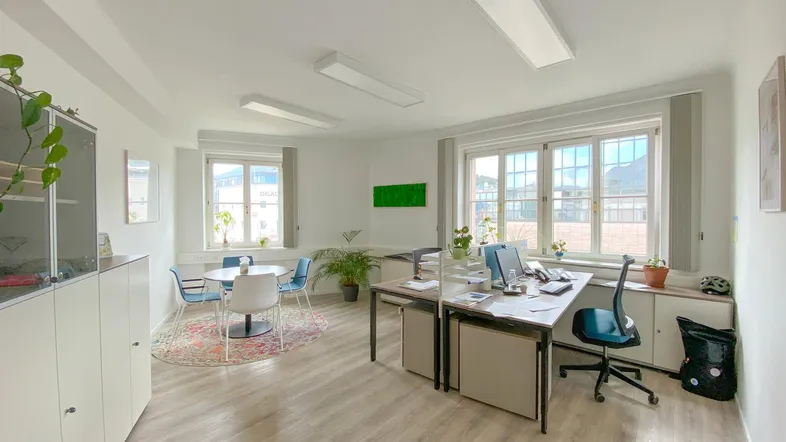 Helles und geräumiges Büro mit mehreren Arbeitsplätzen, Besprechungsecke und großen Fenstern.