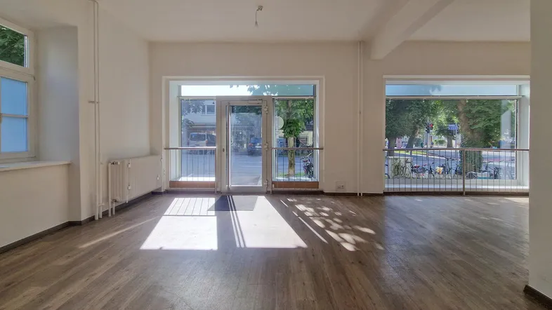 Geräumiger, heller Geschäftsraum mit großen Fenstern und Holzboden, ideal für Laden oder Büro.