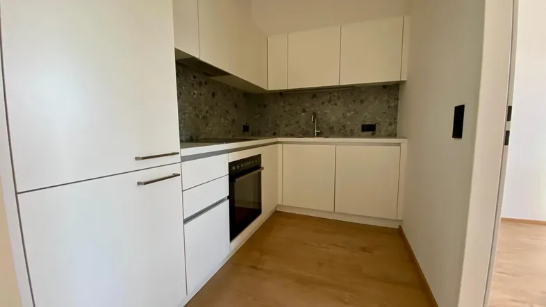 Moderne Einbauküche mit weißen Hochglanzfronten, dunkler Arbeitsplatte und hellem Holzfußboden.