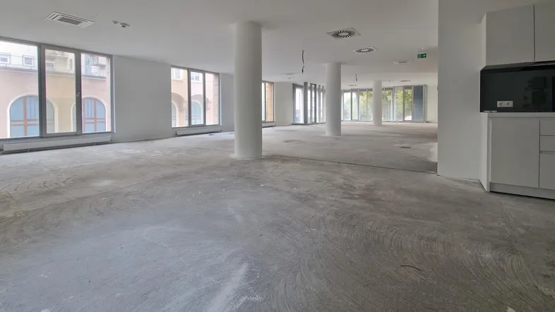 Großer, offener Büroraum mit vielen Fenstern, Säulen und einem unfertigen Betonboden.