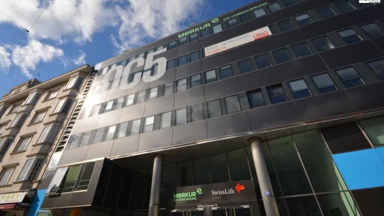 Modernes Bürogebäude mit dunkler Fassade und großen Fenstern unter blauem Himmel, das eine professionelle Atmosphäre ausstrahlt.