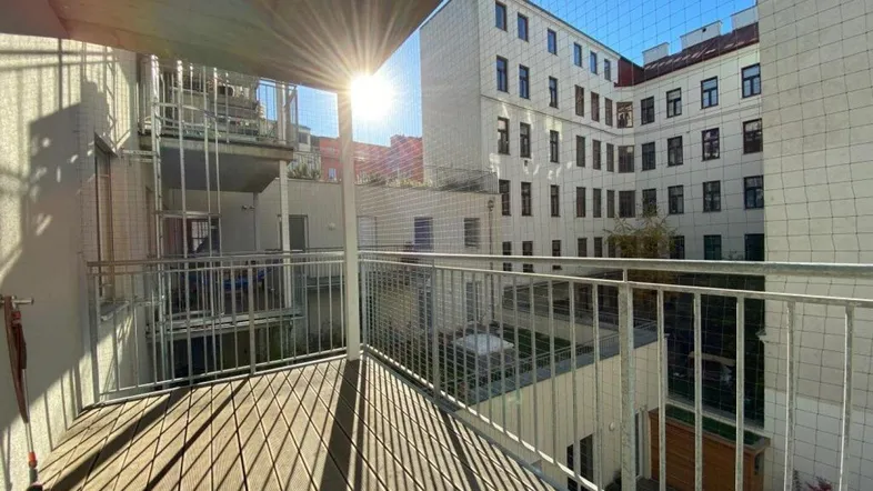 Sonnenbeschienener Balkon mit Holzboden und Blick auf den Innenhof.