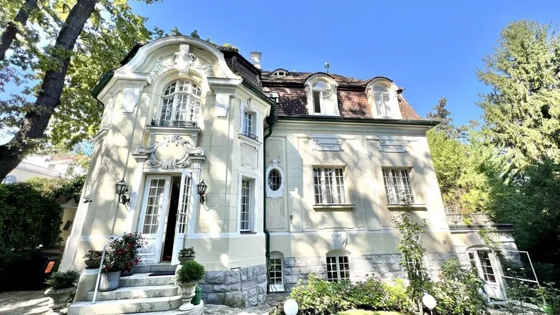 Elegante Villa mit historischer Architektur, umgeben von einem gepflegten Garten unter blauem Himmel.