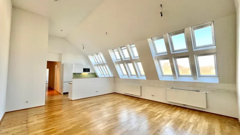 Helles Dachgeschoss-Wohnzimmer mit Holzboden, Dachschrägen und integrierter Küchenzeile.