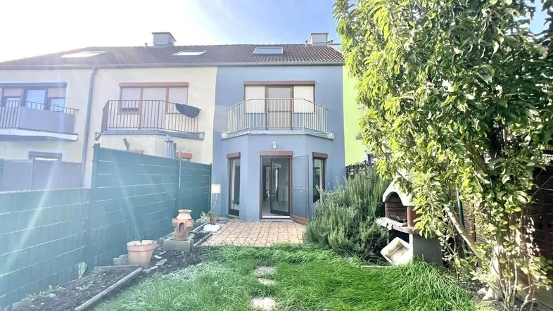 Blick auf den gepflegten Garten mit Grillplatz und die Rückseite des Reihenhauses mit Balkon.
