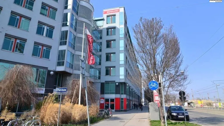 Modernes Bürogebäude mit Glasfassade und mehreren Etagen an einer belebten Straße.