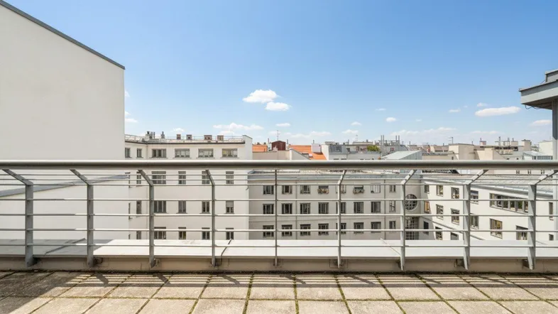 Geräumige Dachterrasse mit Fliesenboden und weitem Blick über die Dächer der Stadt unter blauem Himmel.