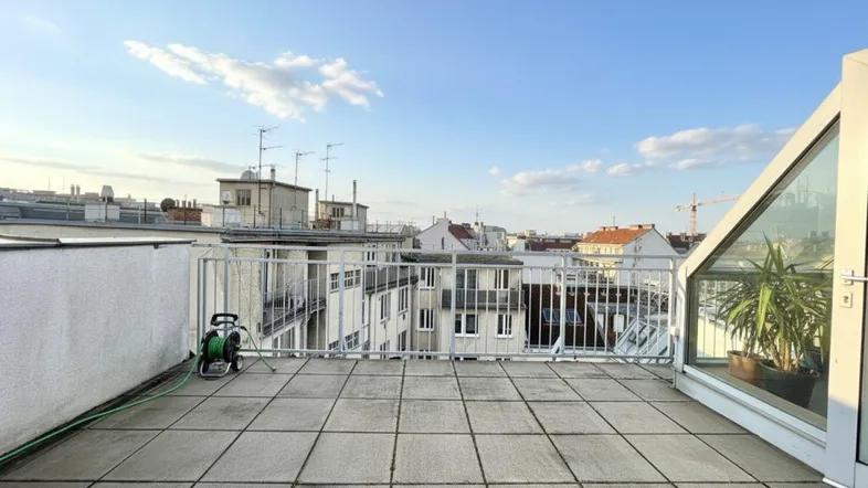 Weitläufige Dachterrasse mit Fliesenboden, umgeben von Stadtgebäuden unter blauem Himmel.