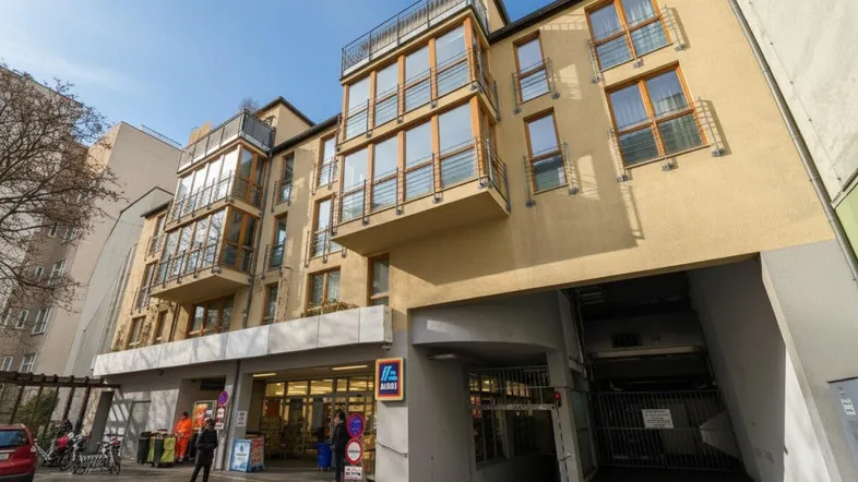 Modernes Mehrfamilienhaus mit Balkonen, großen Fenstern, integriertem Supermarkt und Tiefgaragenzufahrt.