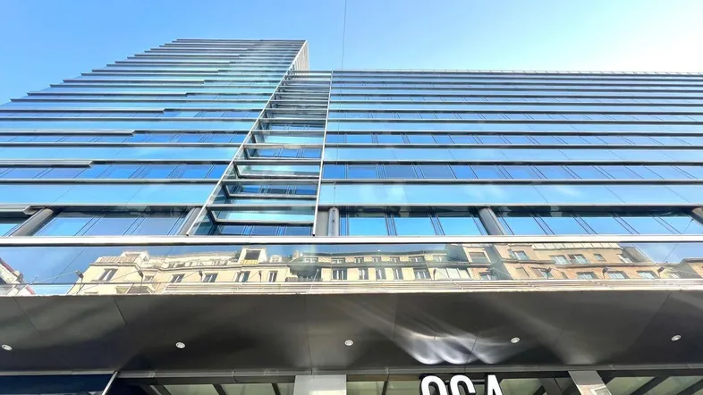 Modernes Hochhaus mit Glasfassade und reflektierenden Fenstern unter blauem Himmel.