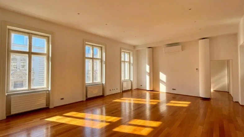 Geräumiger Wohnbereich mit glänzendem Parkettboden, hohen Decken und Klimaanlage in einem Altbau.
