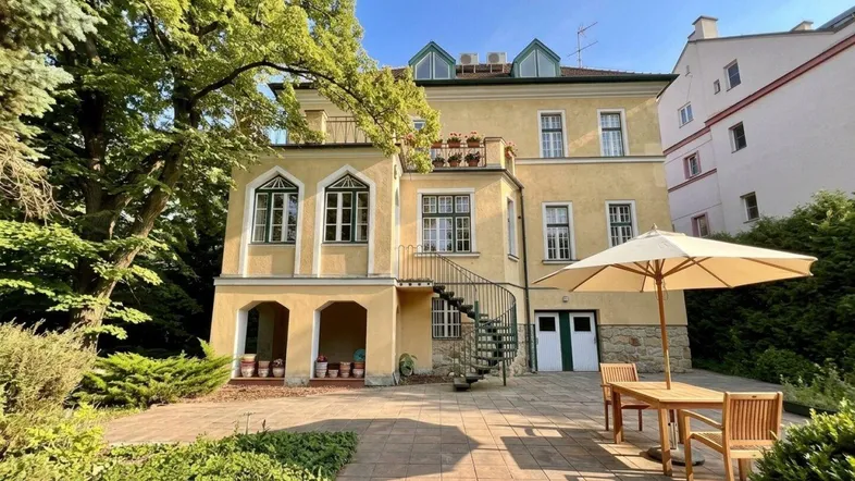 Historisches Gebäude mit großzügiger Terrasse und Gartenbereich, umgeben von altem Baumbestand.