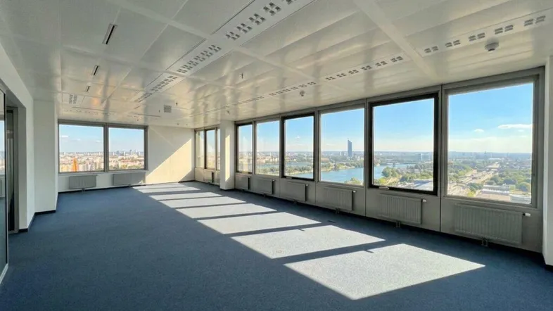 Geräumiges, leeres Büro mit Teppichboden und großen Fenstern, die einen weiten Blick auf die Stadt und das Wasser bieten.
