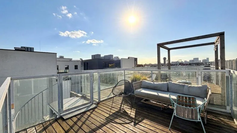 Sonnige Dachterrasse mit Holzboden, Glasgeländer und bequemen Loungemöbeln, ideal zum Entspannen.
