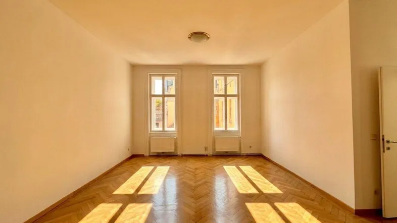 Helles Zimmer mit Fischgrätparkett und viel Tageslicht durch zwei hohe Fenster.