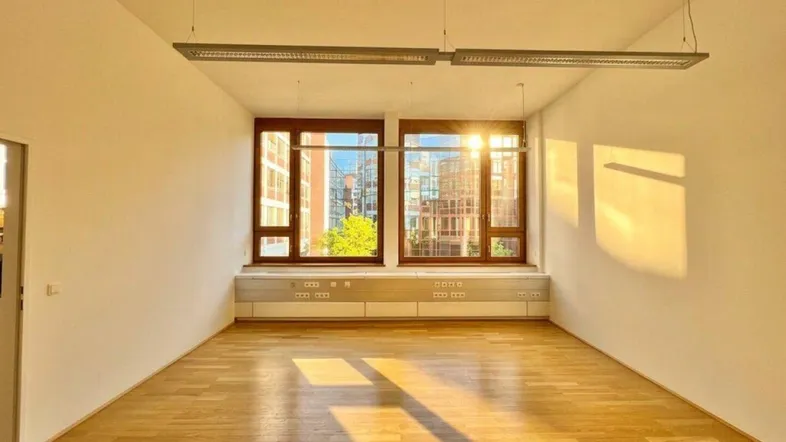 Heller Büroraum mit großen Fenstern, Holzboden und viel natürlichem Licht, ideal für Arbeitsbereiche.