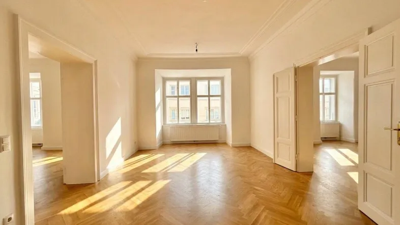 Heller Wohnraum mit Fischgrätparkett, hohen Decken und viel natürlichem Licht durch große Fenster.