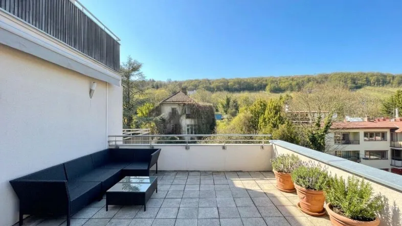 Geräumige Sonnenterrasse mit bequemen Loungemöbeln und weitem Blick ins Grüne unter blauem Himmel.