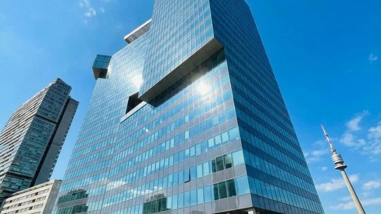 Modernes Hochhaus mit beeindruckender Glasfassade unter strahlend blauem Himmel in urbaner Umgebung.
