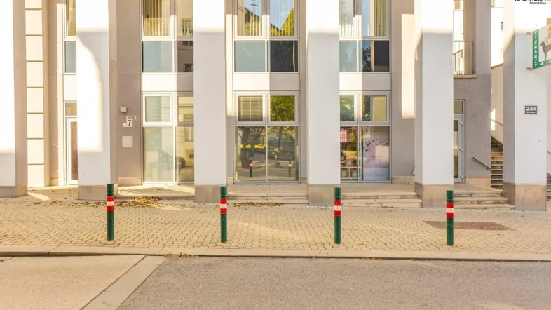 Moderne Fassade eines Geschäftsgebäudes mit großen Fenstern, weißen Säulen und mehreren Eingängen.