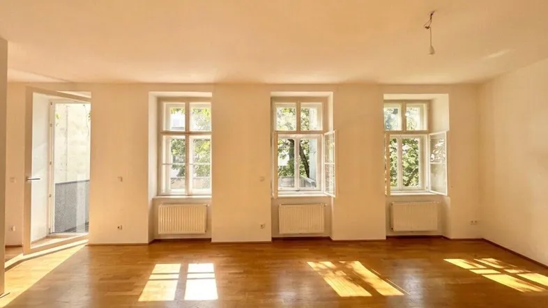 Helles Wohnzimmer mit Parkettboden und mehreren Fenstern, die viel Sonnenlicht hereinlassen.