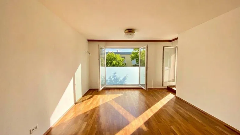 Helles Wohnzimmer mit Parkettboden und Zugang zu einem Balkon.