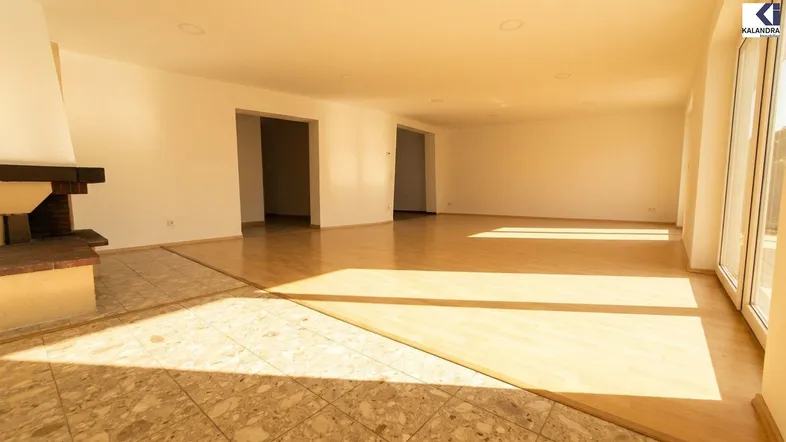 Geräumiges Wohnzimmer mit hellem Parkettboden, Kamin und viel natürlichem Licht durch große Fenster.