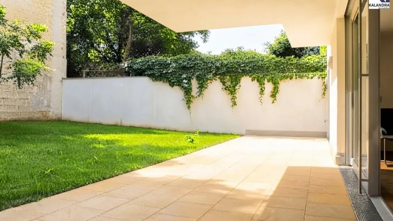 Große gepflasterte Terrasse mit angrenzendem Rasenbereich und begrüntem Zaun.