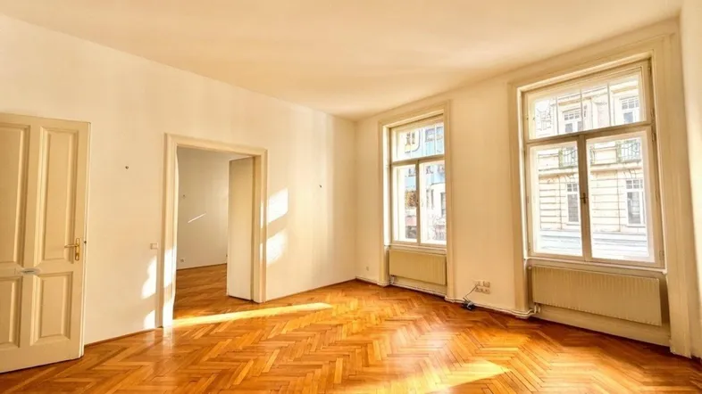 Geräumiges Wohnzimmer mit Fischgrätparkett, hohen Fenstern und viel natürlichem Licht.