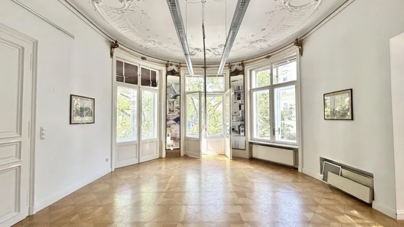 Geräumiges Wohnzimmer mit Fischgrätparkett, hohen Decken und reich verzierten Stuckelementen.