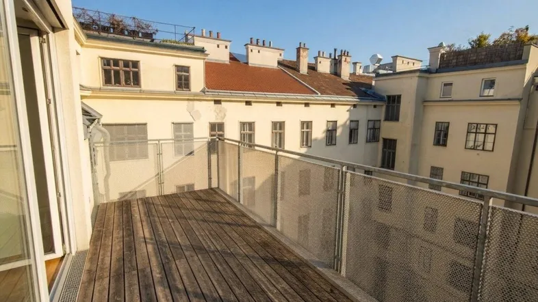 Geräumiger Balkon mit Holzboden und Metallgeländer, bietet Blick auf den Innenhof.