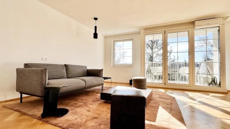 Helles Wohnzimmer mit Parkettboden, bequemer Couch und Zugang zum Balkon.