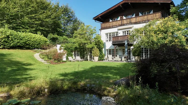 Großzügiger Gartenbereich mit Teich, umgeben von Bäumen und einer möblierten Terrasse am Haus.