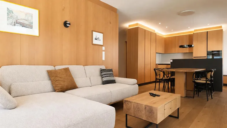 Moderner offener Wohn- und Essbereich mit Holzakzenten, beigem Sofa und integrierter Küche.