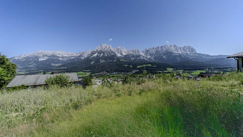 Panoramablick auf die majestätischen Berge und das Tal mit Häusern unter klarem blauem Himmel.