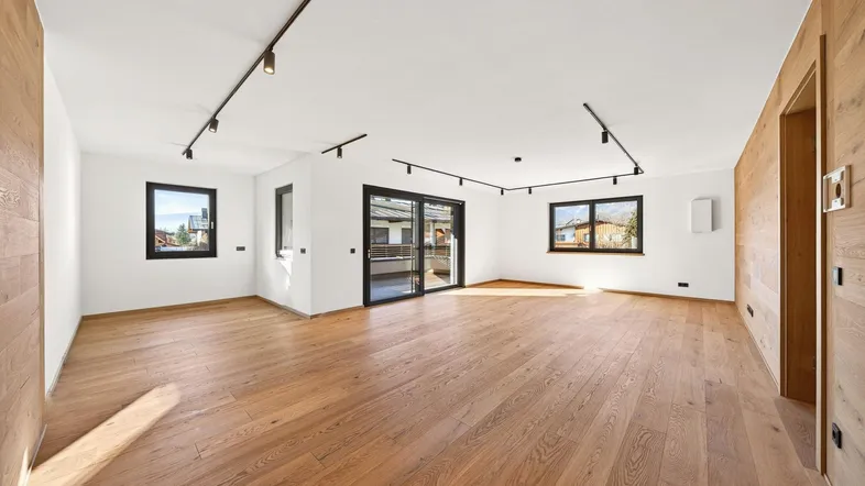 Geräumiges, helles Wohnzimmer mit Holzboden, großen Fenstern und Zugang zum Balkon.