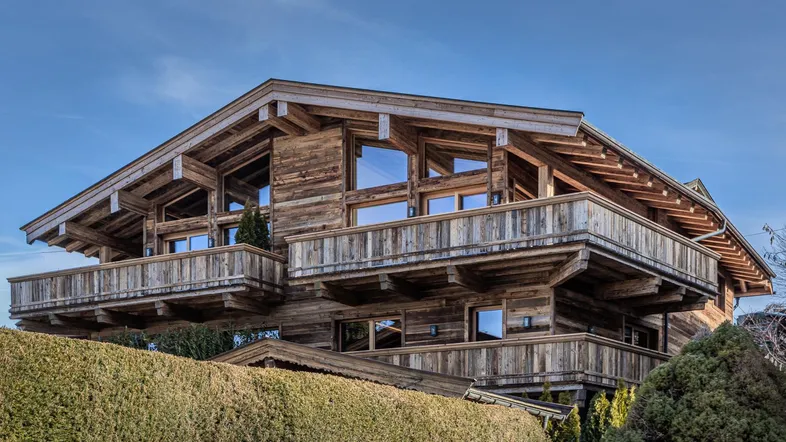 Attraktives Holzchalet mit mehreren Balkonen und traditioneller alpiner Architektur unter blauem Himmel.